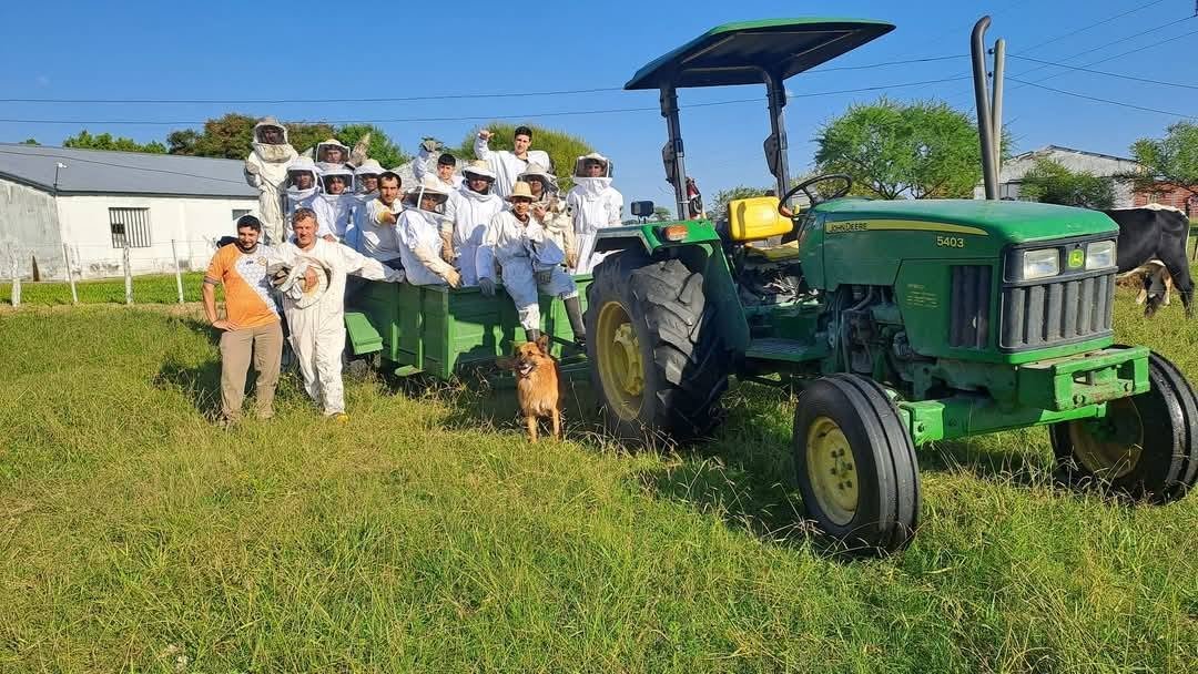 Grupo de estudiantes con trajes de apicultor arriba de un acoplado tirado por tractor